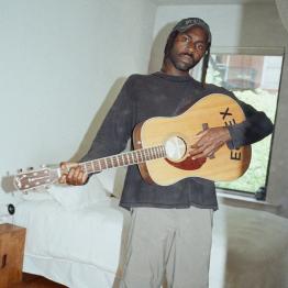 Dev Hynes holding a guitar