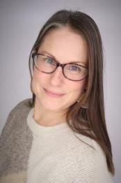 A photo of a woman with glasses in front of a gray background