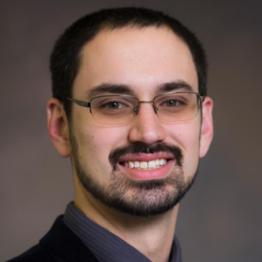 A photo of man with a beard in front of a grey background