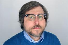 A photo of a man with glasses in front of a grey background