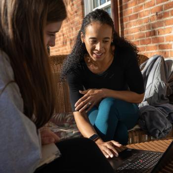 Student and staff member look at a laptop screen during meeting on McGuffey porch. 