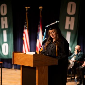 Student Bailey Ray stands in a graduation robe at a podium at commencement