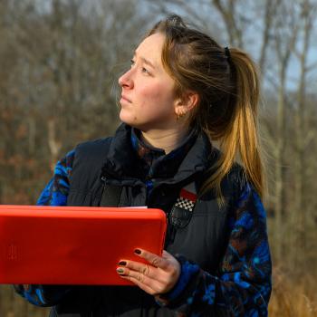 An image of Elizabeth Savitski outside in the field, studying the skyline and inputing information into a tablet.