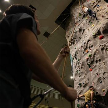 A belayer keeps a hold of the rope as a climber makes their way up a 36-foot-tall rock-climbing wall 