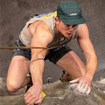 shot from top of climbing wall shows man reaching to climb higher 