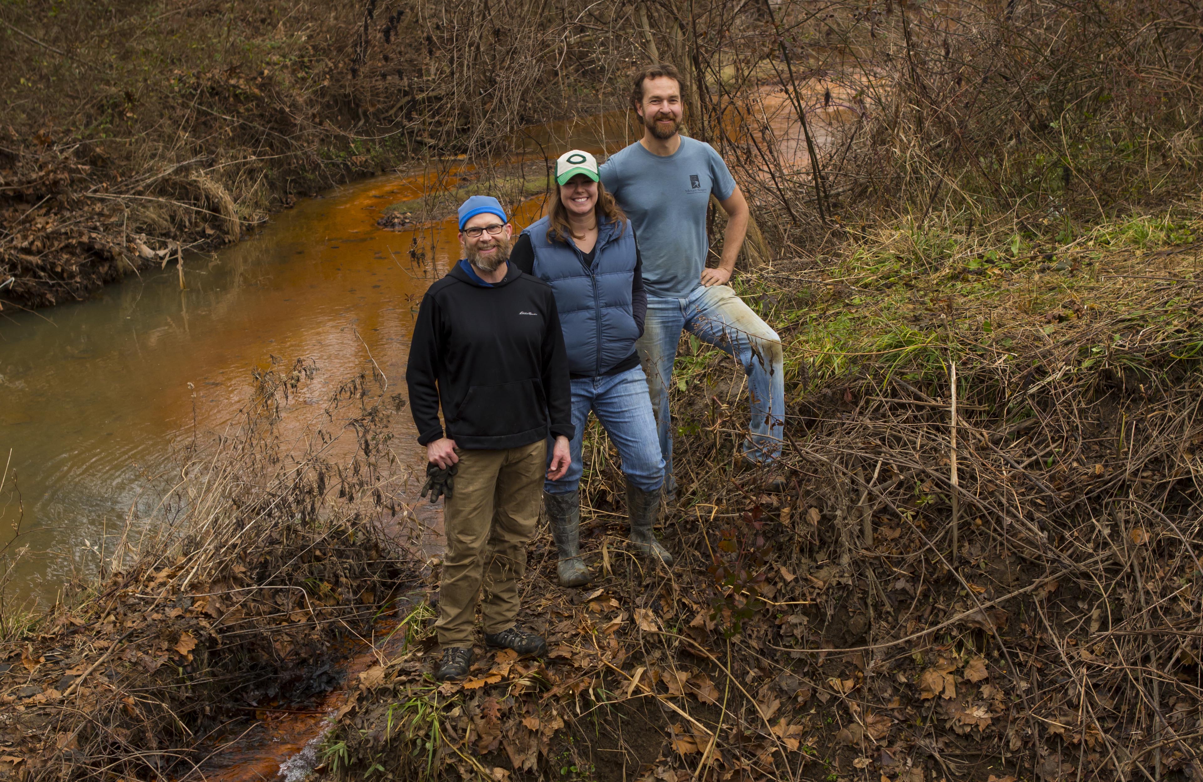 John Sabraw, Michelle Shively, and Guy Riefler pose with a creek behind them.