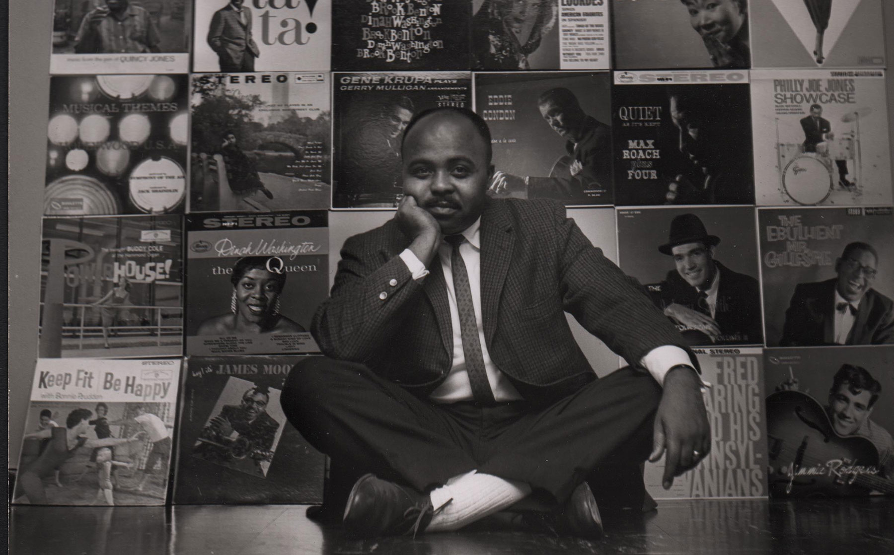 Chuck Stewart sitting in front of a wall of album covers he had taken