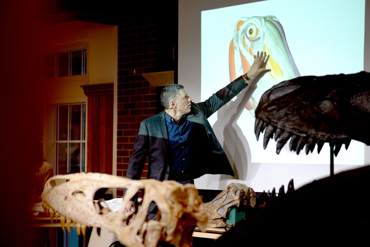 Larry Witmer presents at a science cafe with a dinosaur skull in the forefront