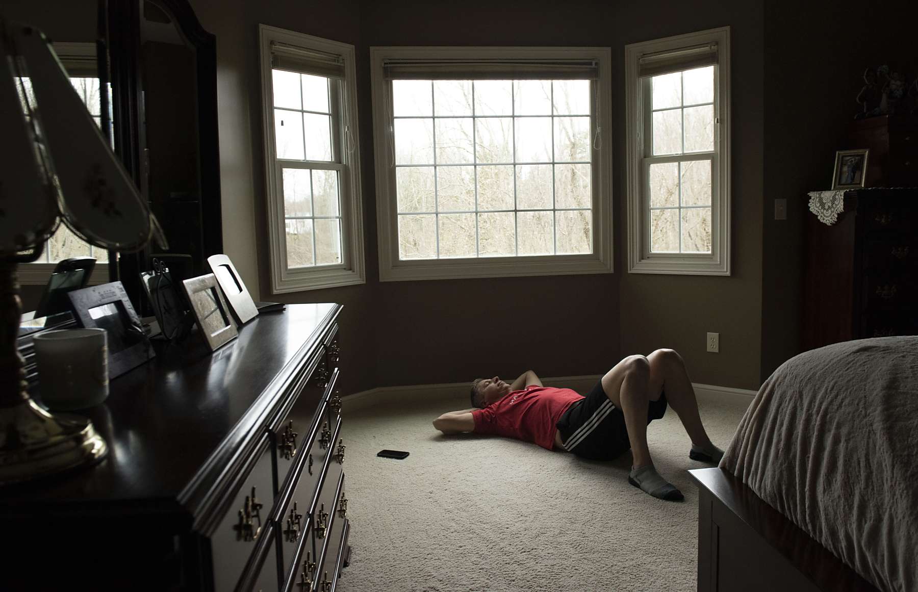 A man lying on the floor of a wide room in front of large windows