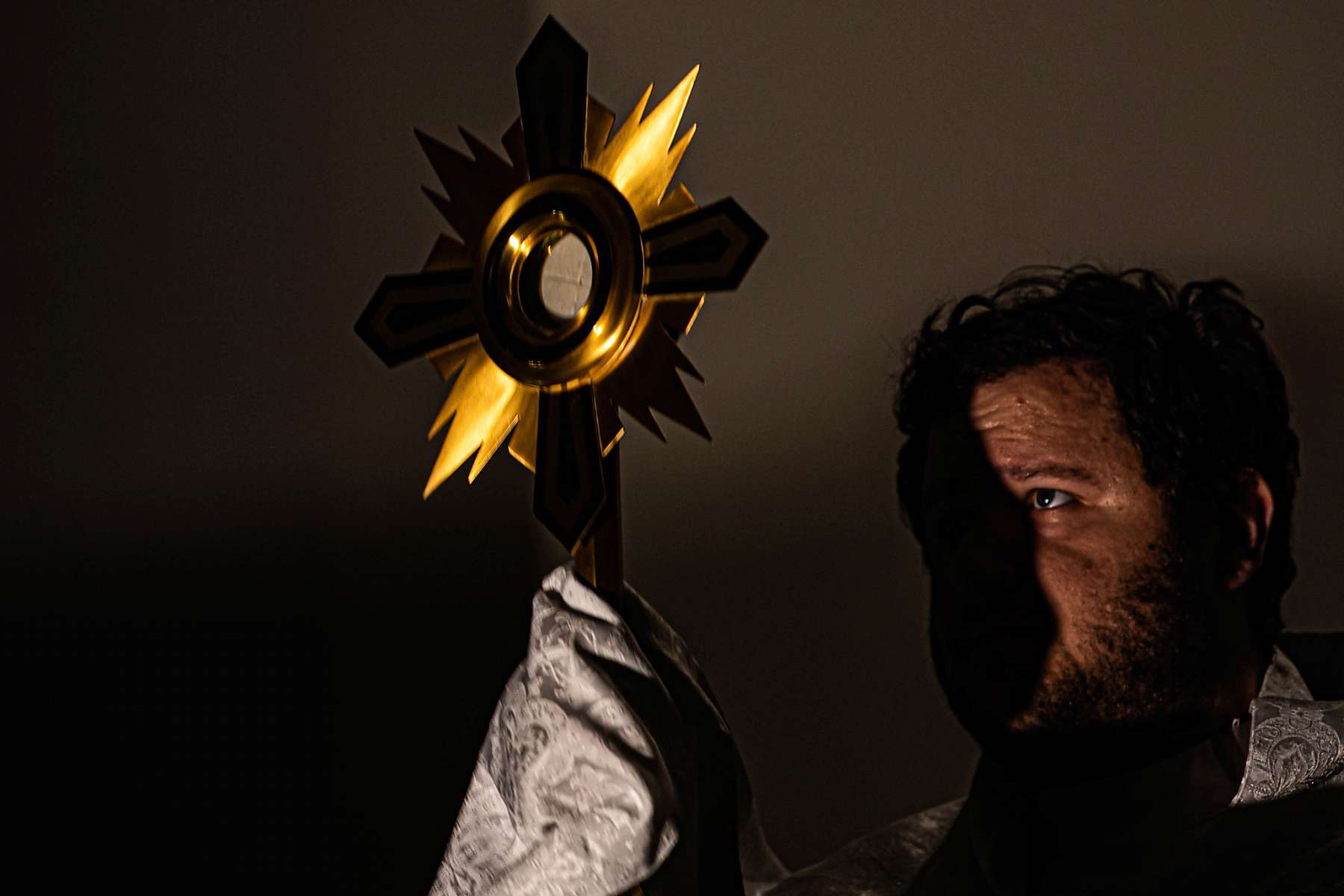 A golden crucifix blocks the light from a man's face