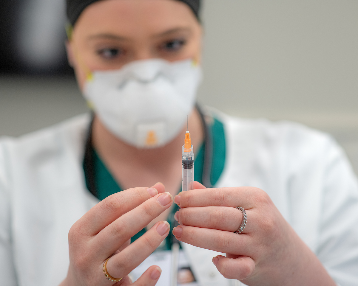 A masked person handles a vial of something