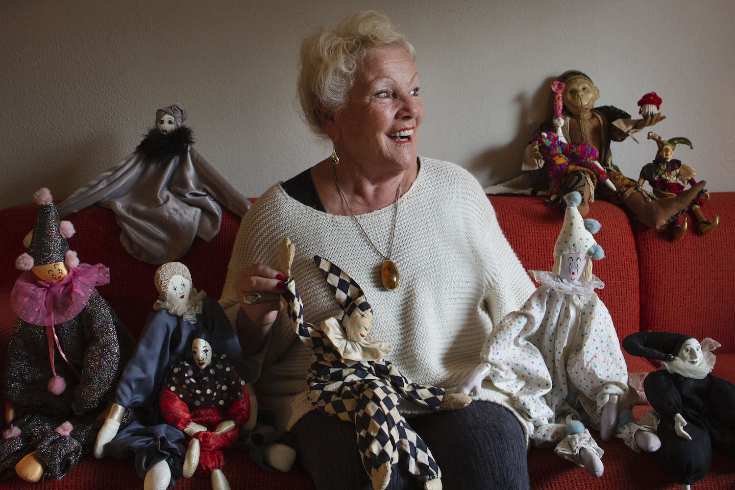 Tilly Berghege smiles around various dolls she has created through the years while sitting on a couch.