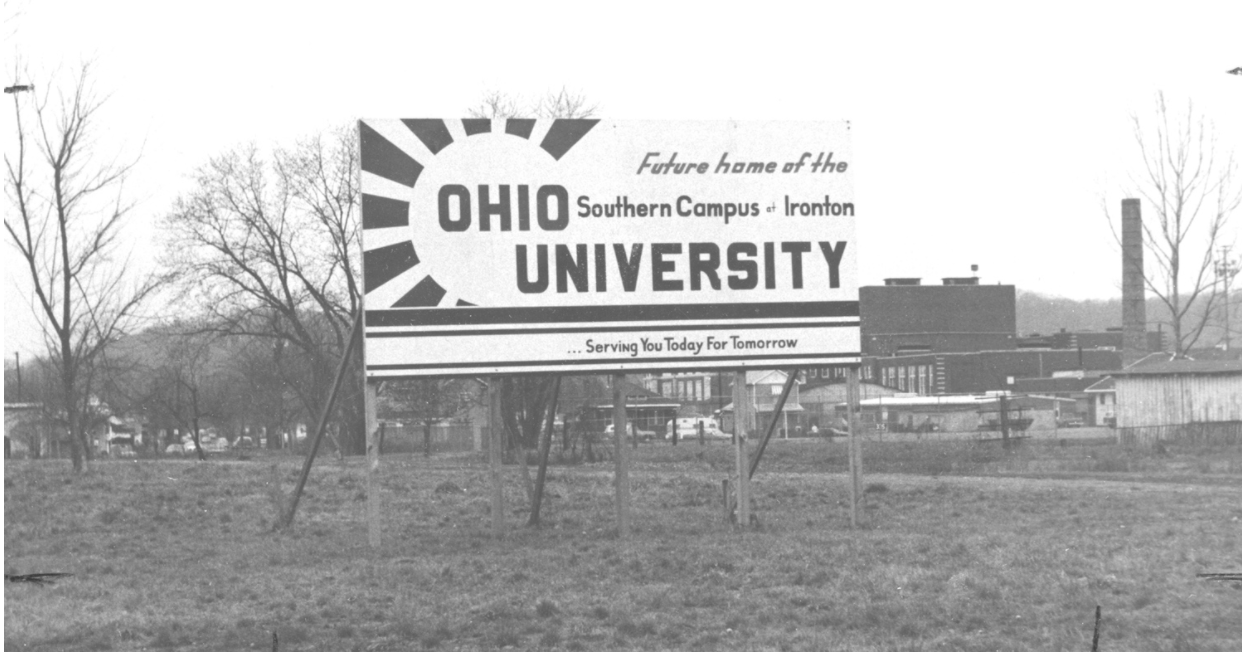 Une photo en noir et blanc d'un vieux panneau d'affichage qui lit "Future maison du campus sud de l'Université de l'Ohio à Ironton ... Vous servir aujourd'hui pour demain"
