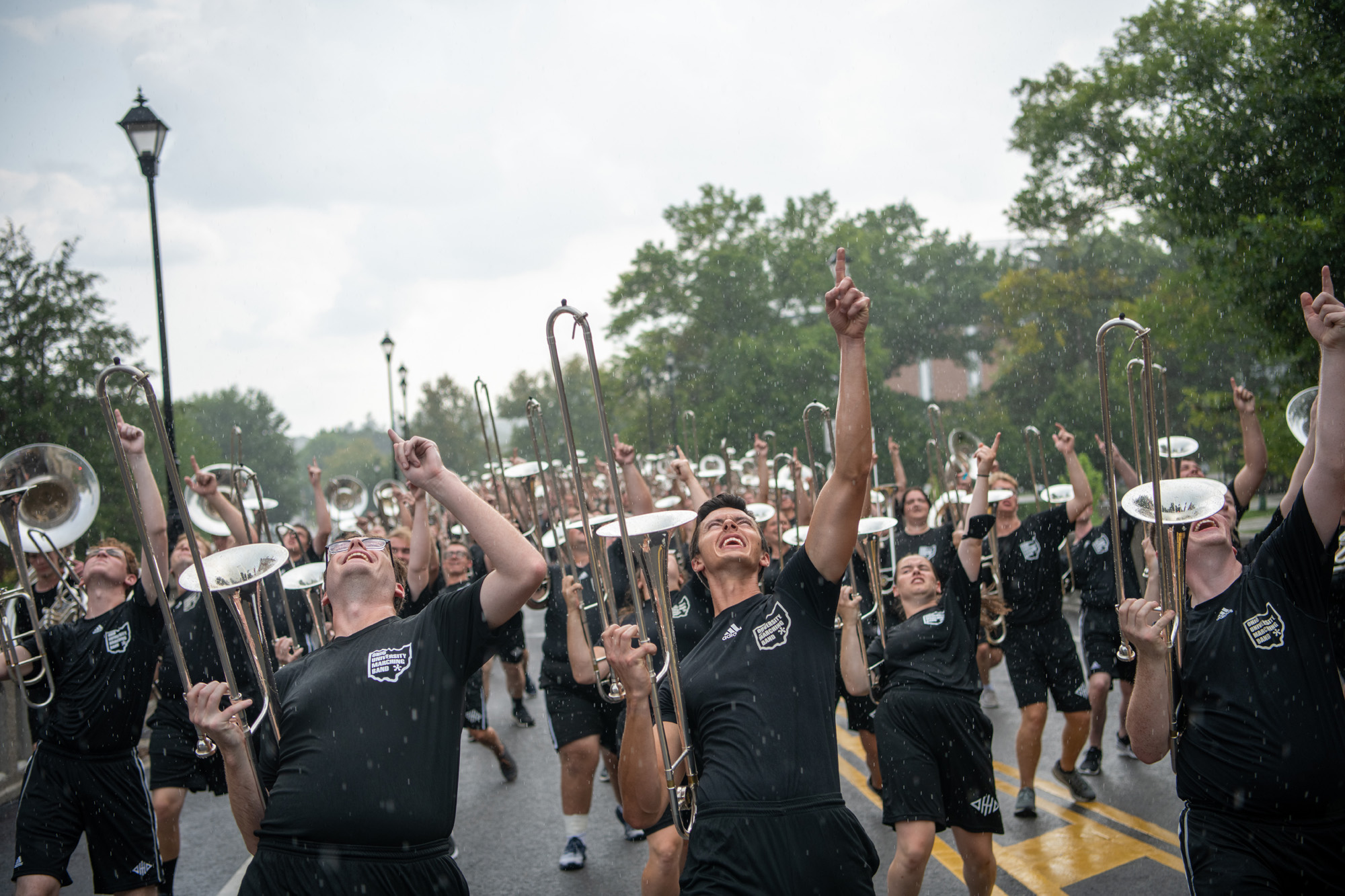 The OHIO Marching 110 enthusiastically play and march down a brick street in the rain