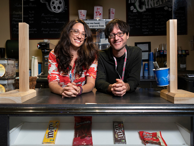 Two visiting filmmakers pose for a picture and smile behind a movie concession stand