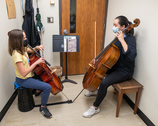 A student teaches a young girl the cello