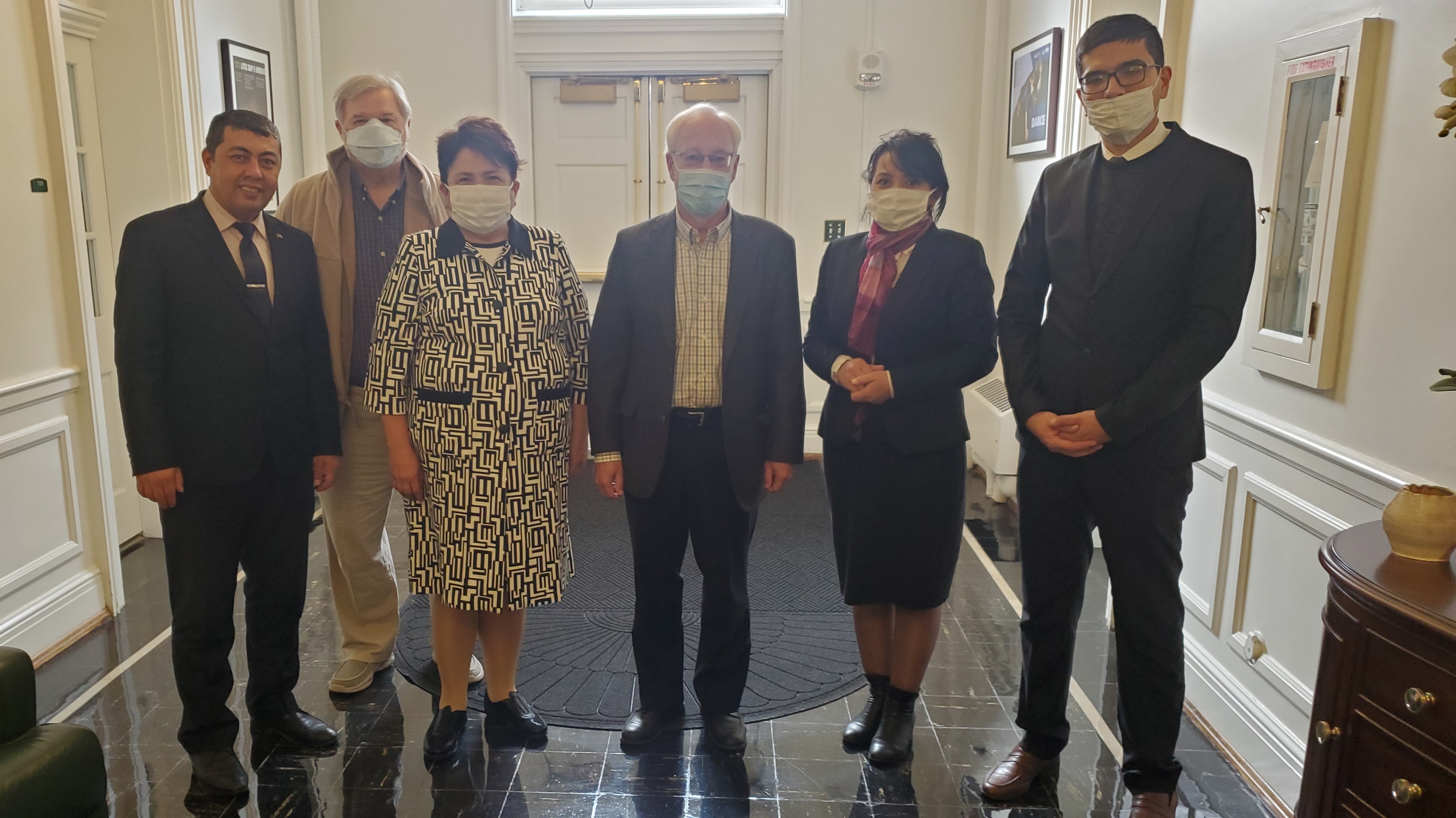 Six people stand together in a hallway with masks on for a picture