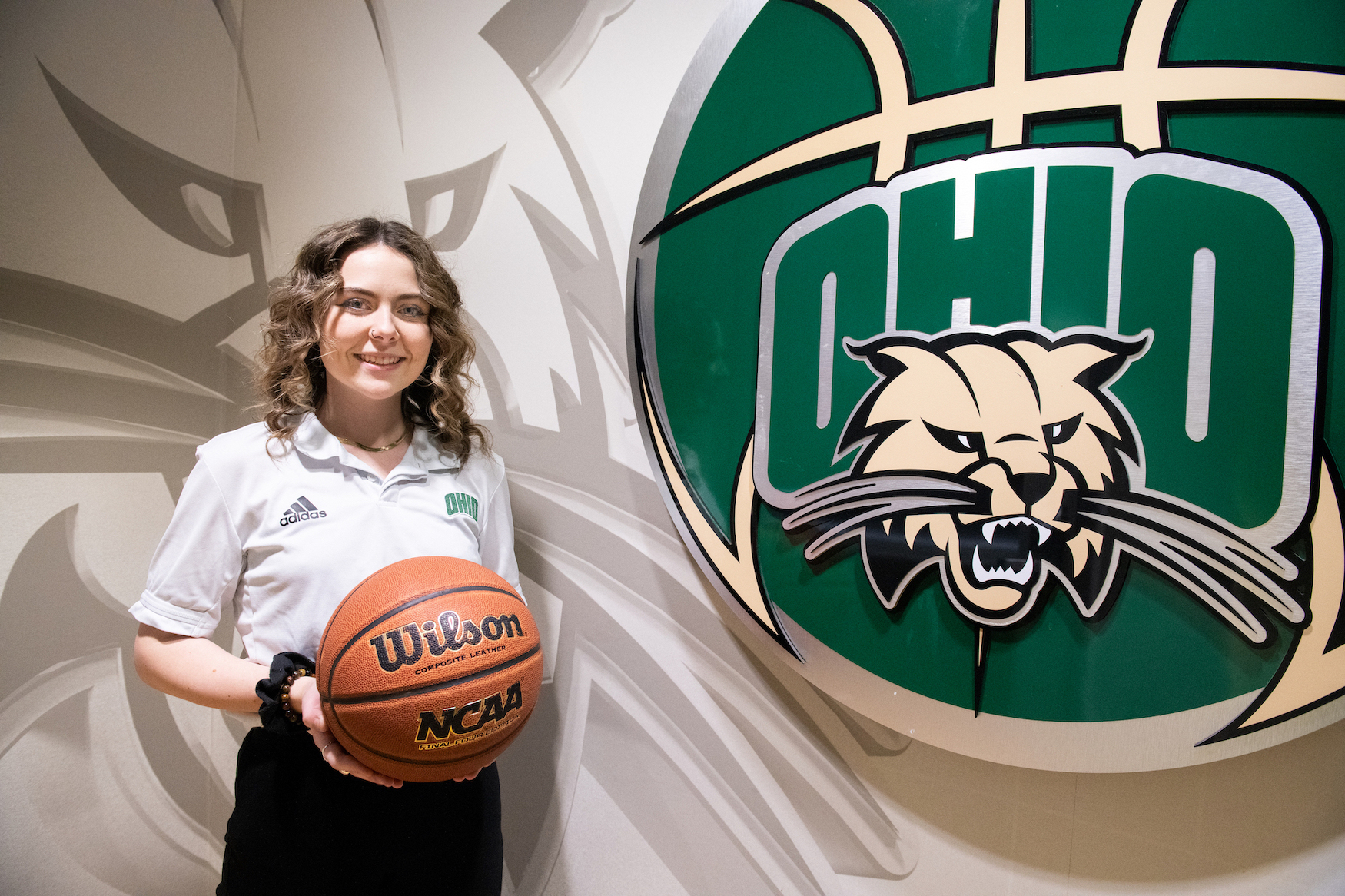 Jess North poses with a basketball in her hands by an Ohio University basketball sign