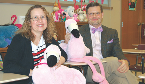 Tracy and her husband sit in a classroom with stuffed flamingos
