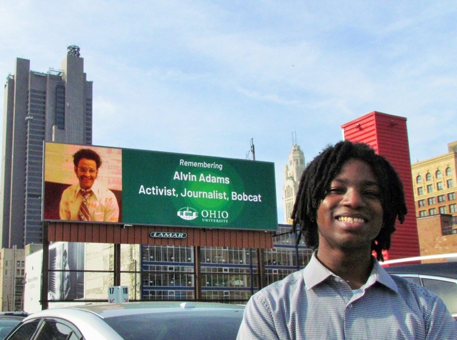 Micah Fluellen is shown in front of a billboard he designed honoring Alvin Adams