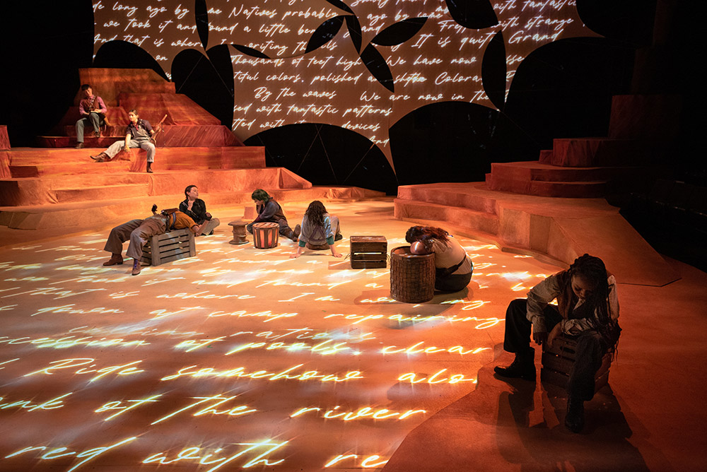 Actors sitting on a stage that has projected text and sunset-colored lights