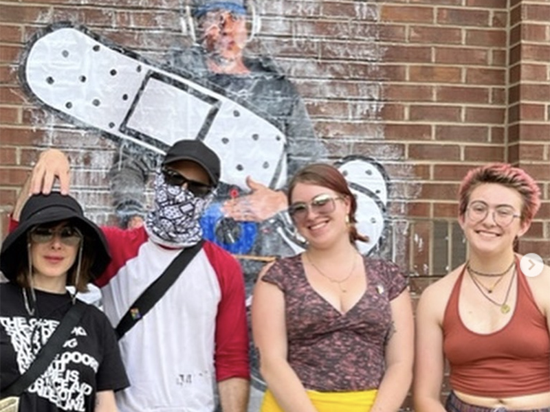 Student assistants stand in front of mural artwork
