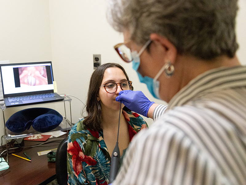 Clinician examines student's vocal chords using a laryngoscope.