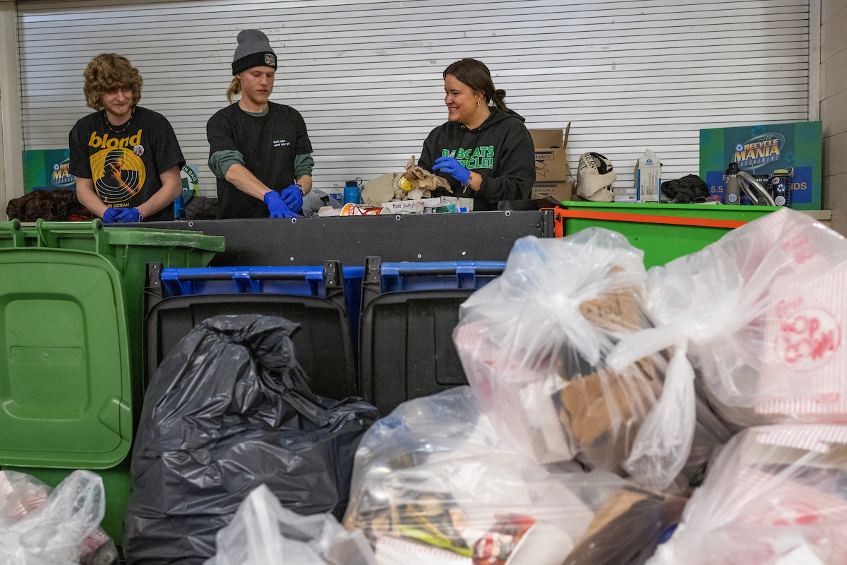 Three students work to sort waste into compost, recycling and trash bins in the Convocation Center