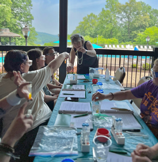 Dr. Jennifer Hines leads the workshop for science teachers, with the beautiful sunny day in the background and teachers at tables in the foreground.