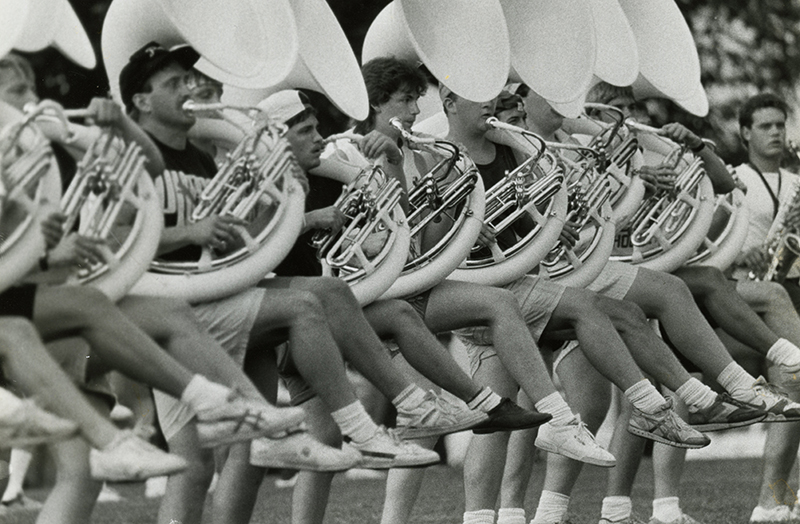 Archival image of Marching 110 sousaphone players high stepping during practice