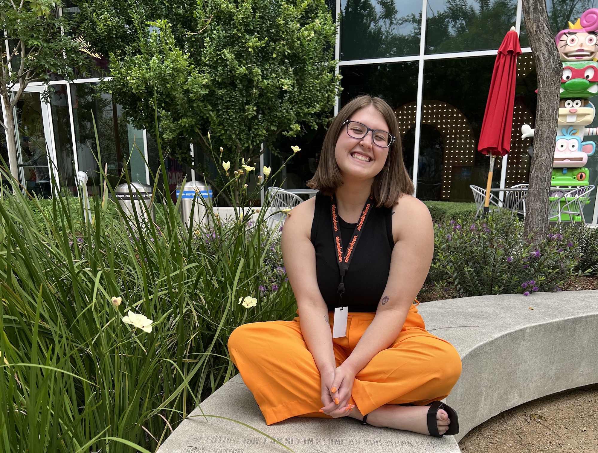 Allison Irey sits criss-crossed on an outside bench at Nickelodeon's campus, with character statues behind her