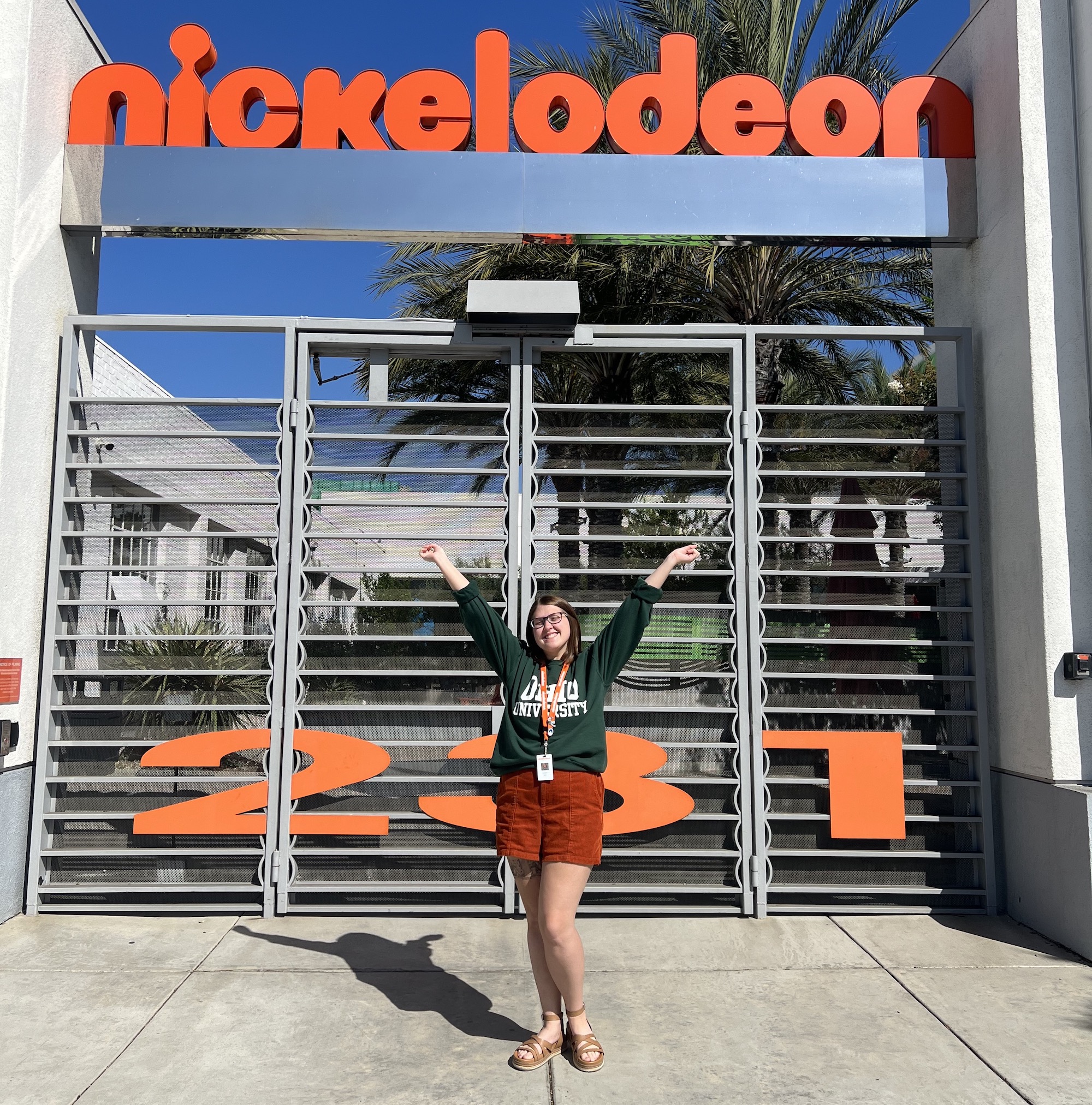Allison Irey poses with her hands up, wearing an Ohio University sweatshirt outside of a movie gate with "Nickelodeon" on top.