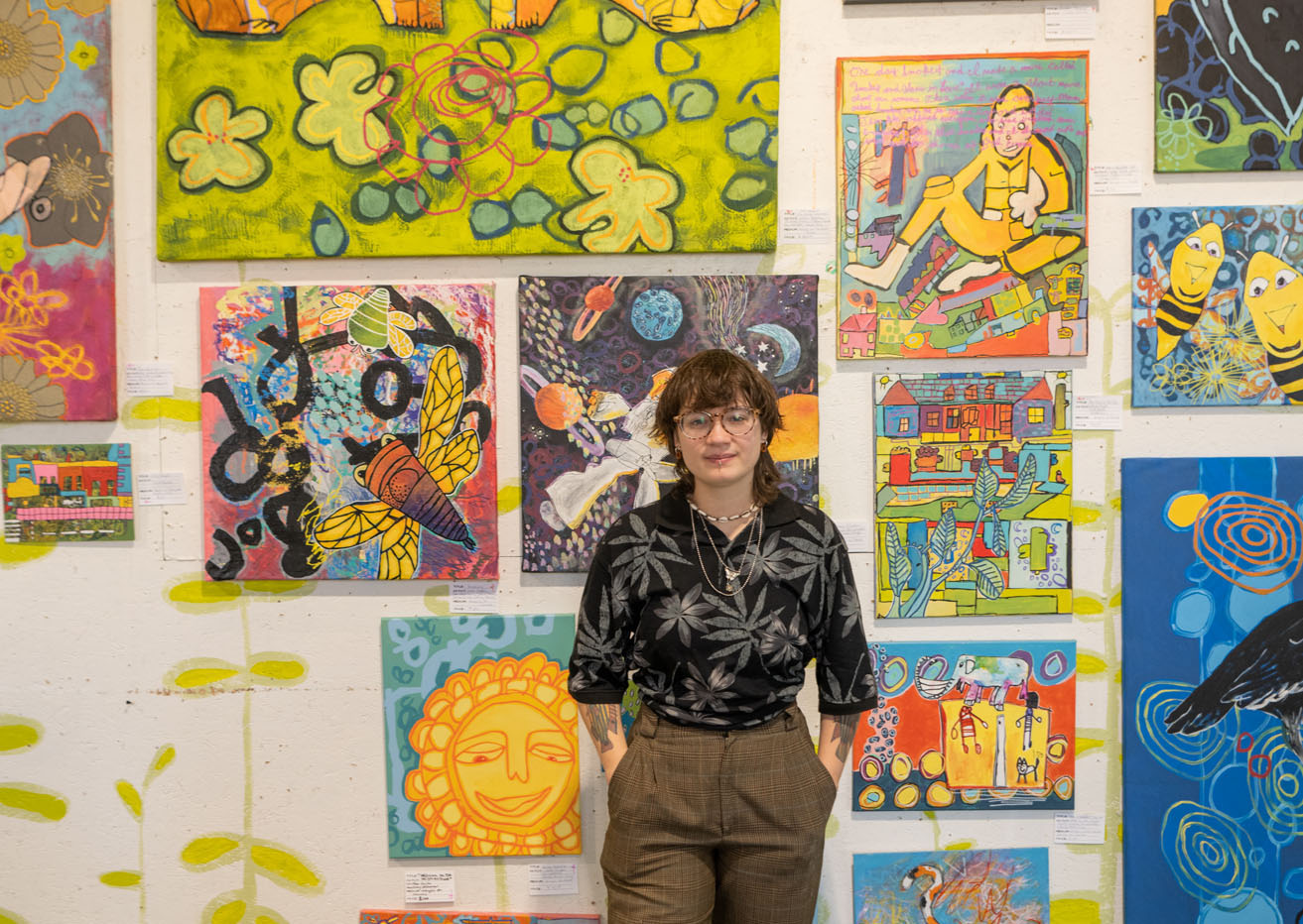 Carrie Sutherford stands in front of paintings in the Passion Works, where she worked as a student in the College of Fine Arts.