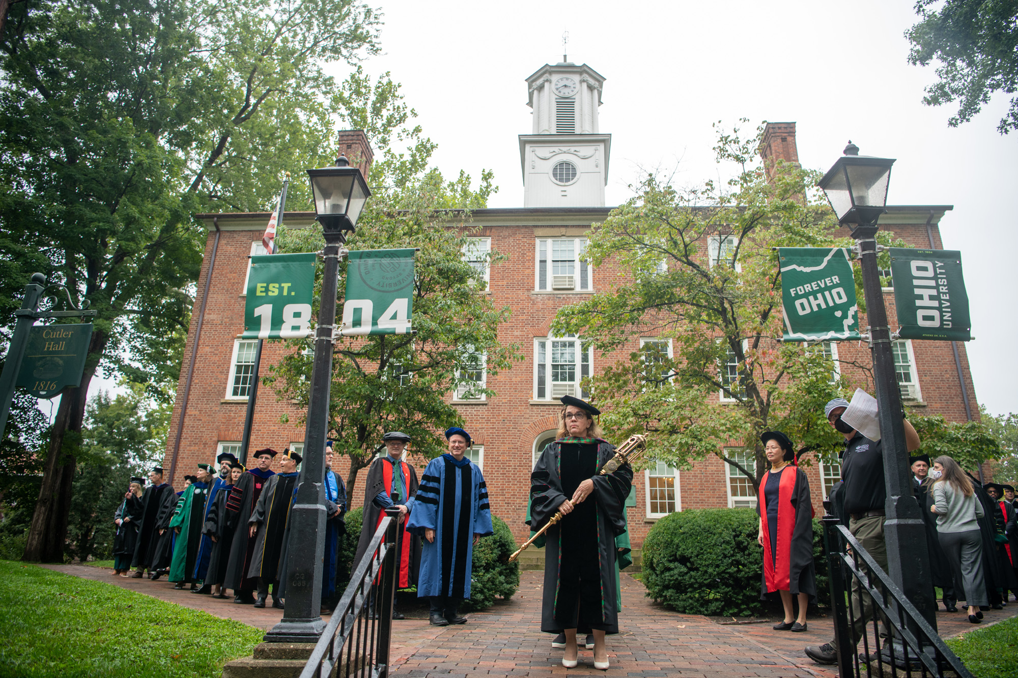 University faculty wear ceremonial robes and stand in front of Cutler Hall for the ceremony