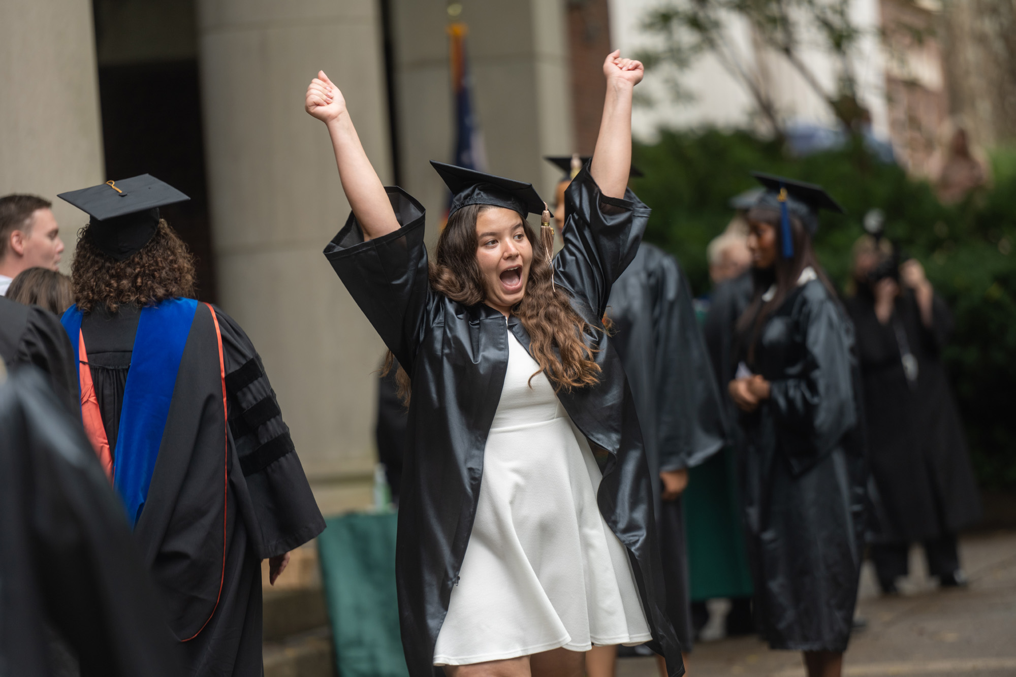 A female graduating student jumps for joy with arms spread