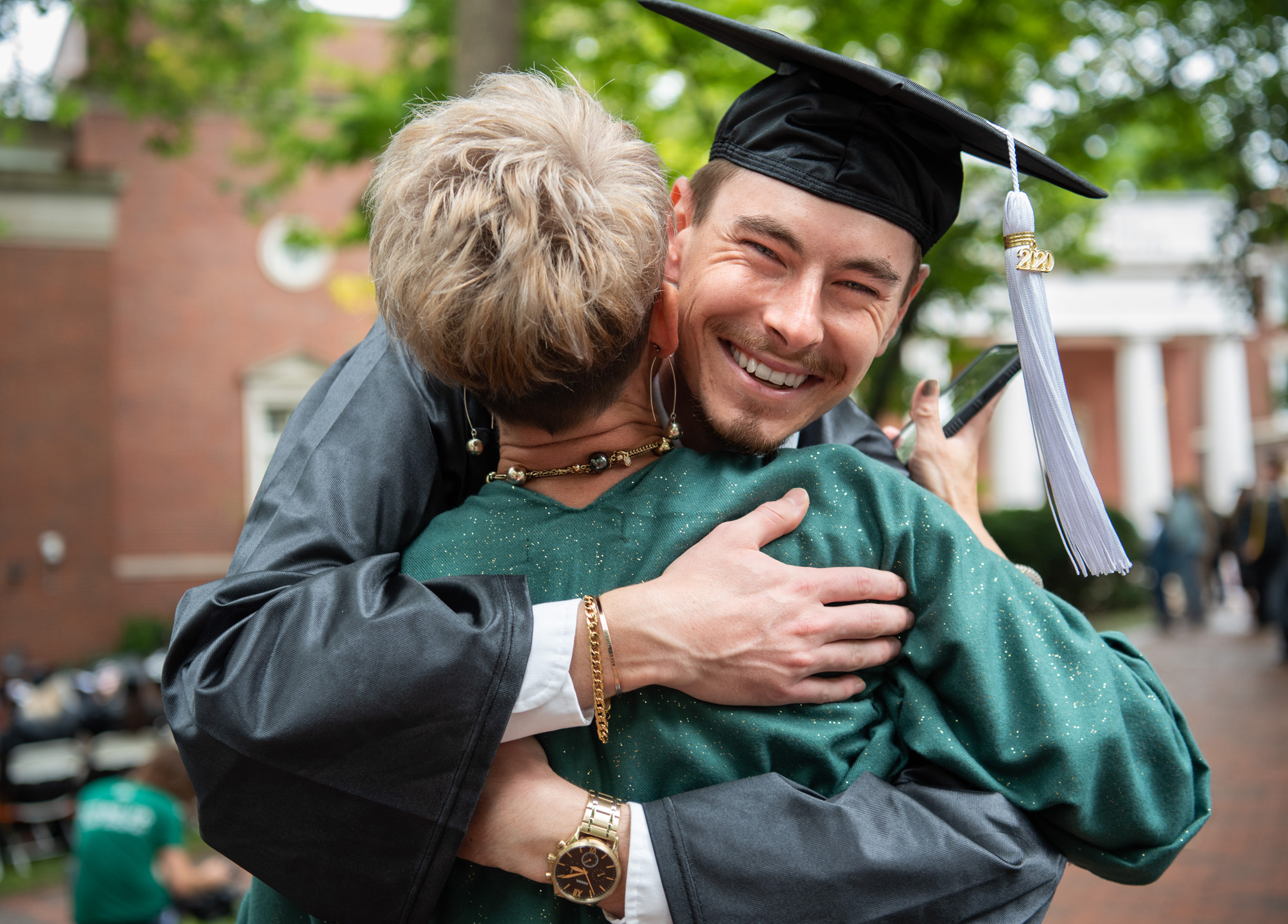 A graduating student smiles as he hugs his mother