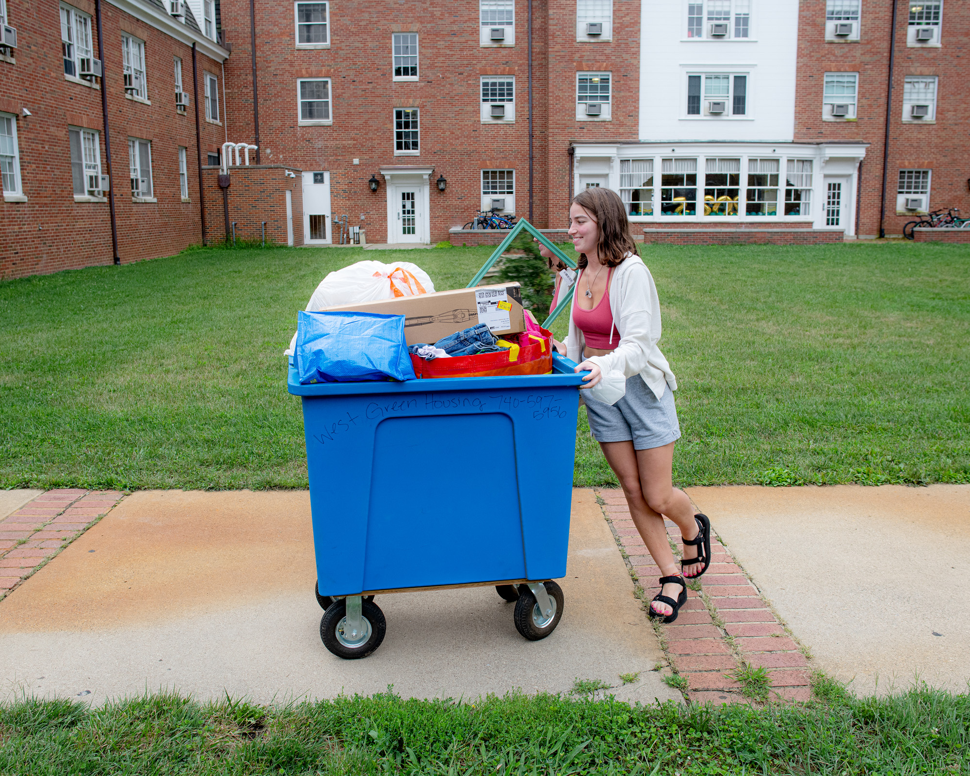 A woman pushes a large cart full of stuff in front of an West Green dormitory