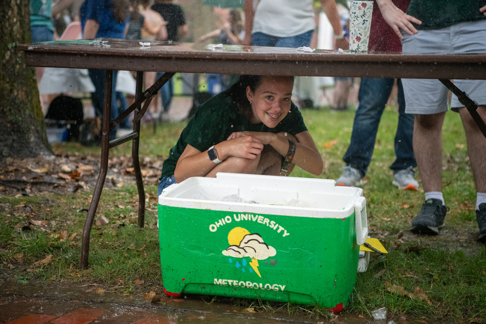 A student smiles while ducking under a table to avoid the rain