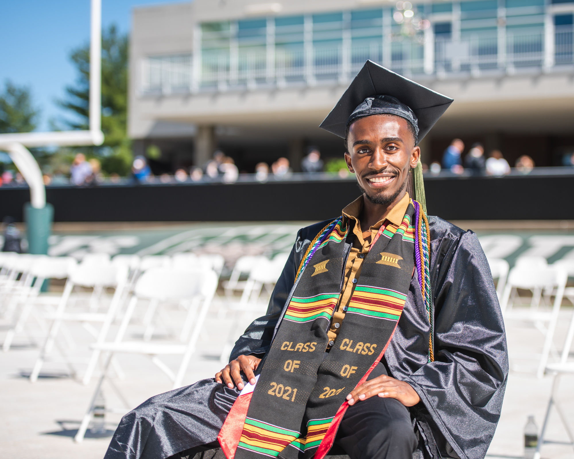 A student dressed in cap and gown for a seated graduation day portrait