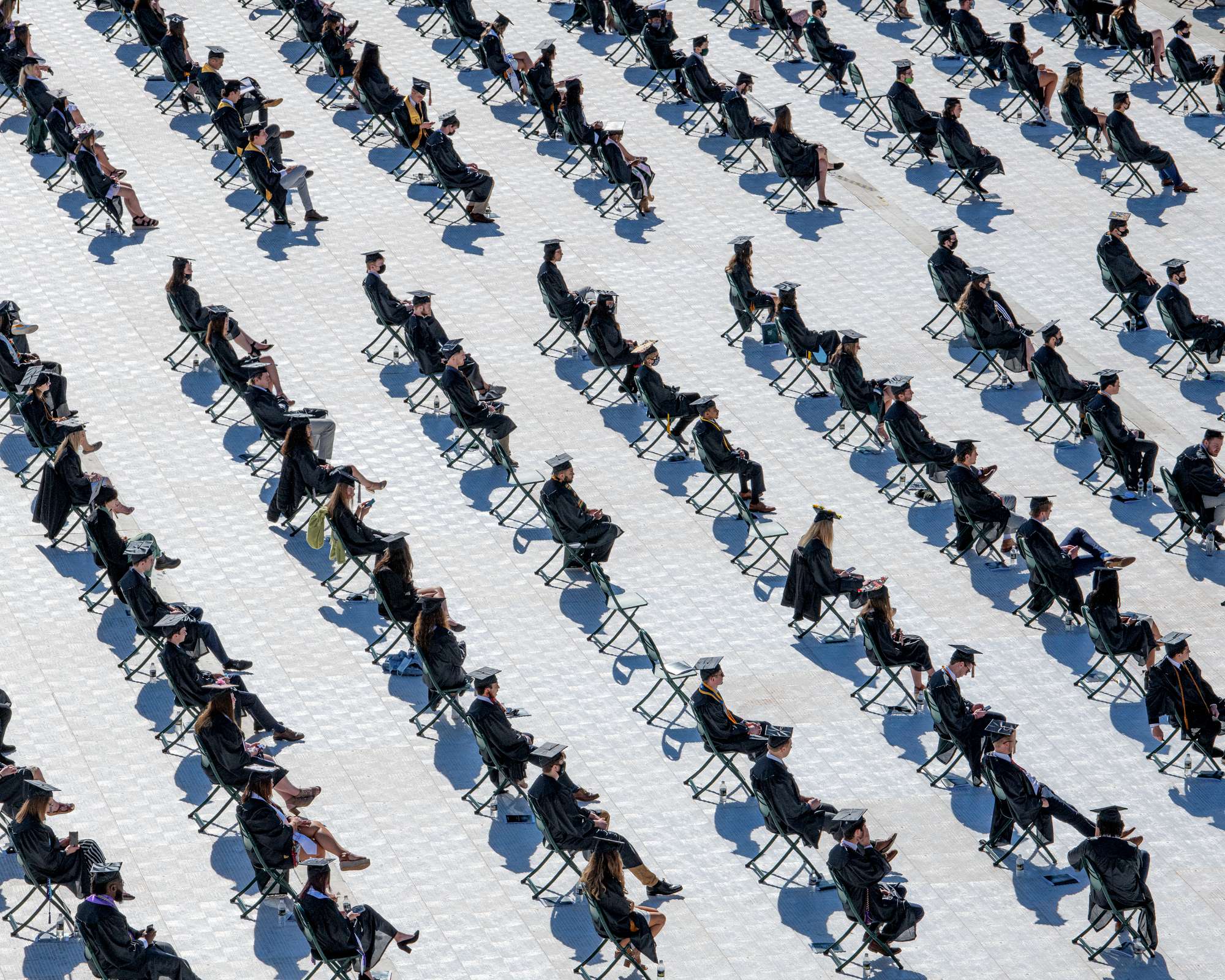 Students seated in caps and gowns on a sparsely filled football field