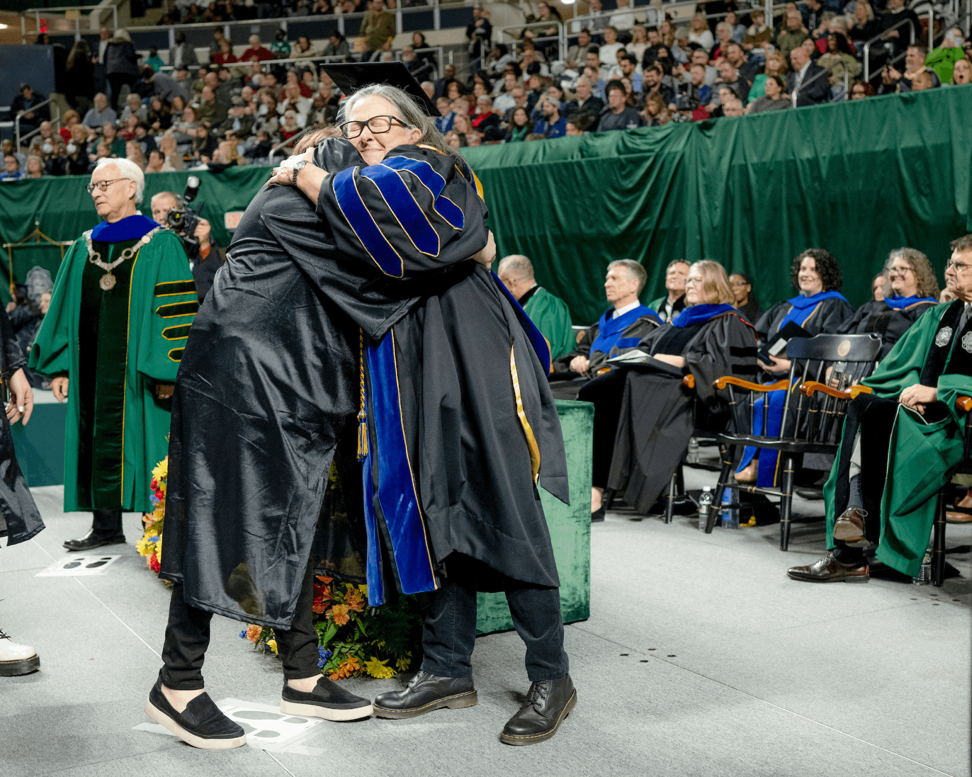 A graduate receives a hug on stage at Fall Commencement.