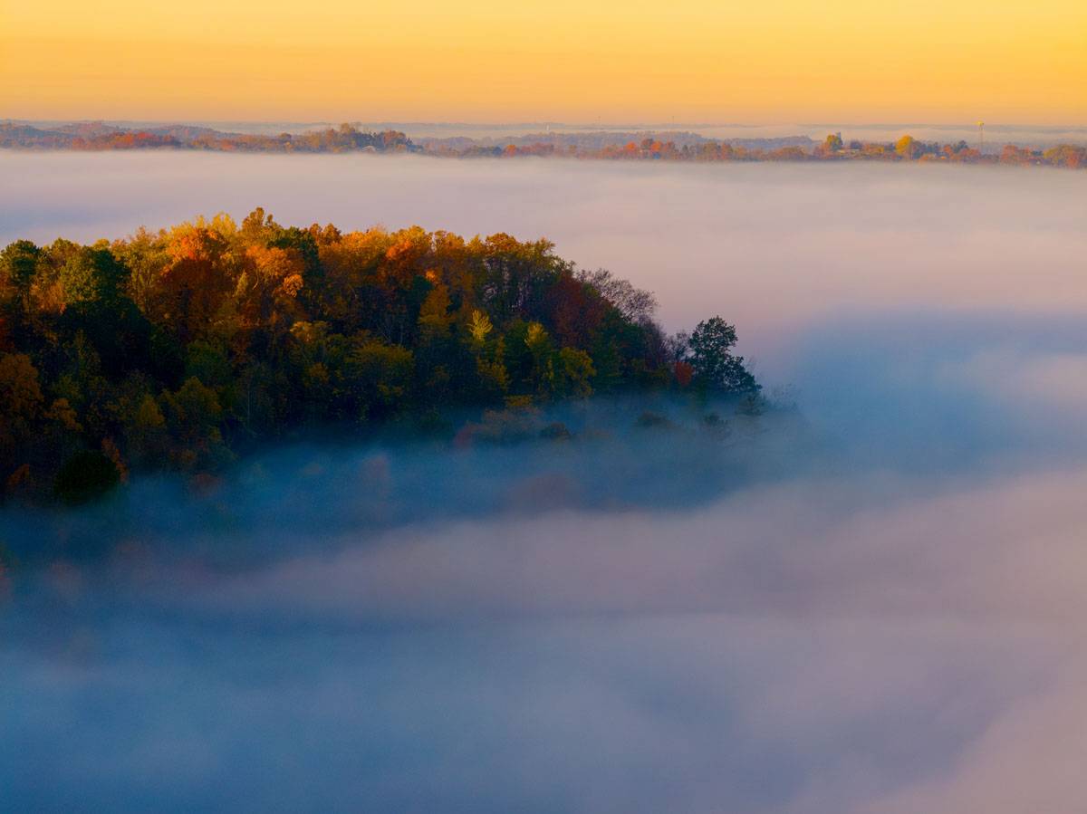 Sunrise illuminates fall colors on the hills surrounding the city of Athens, which is covered by fog near the Hocking River. 