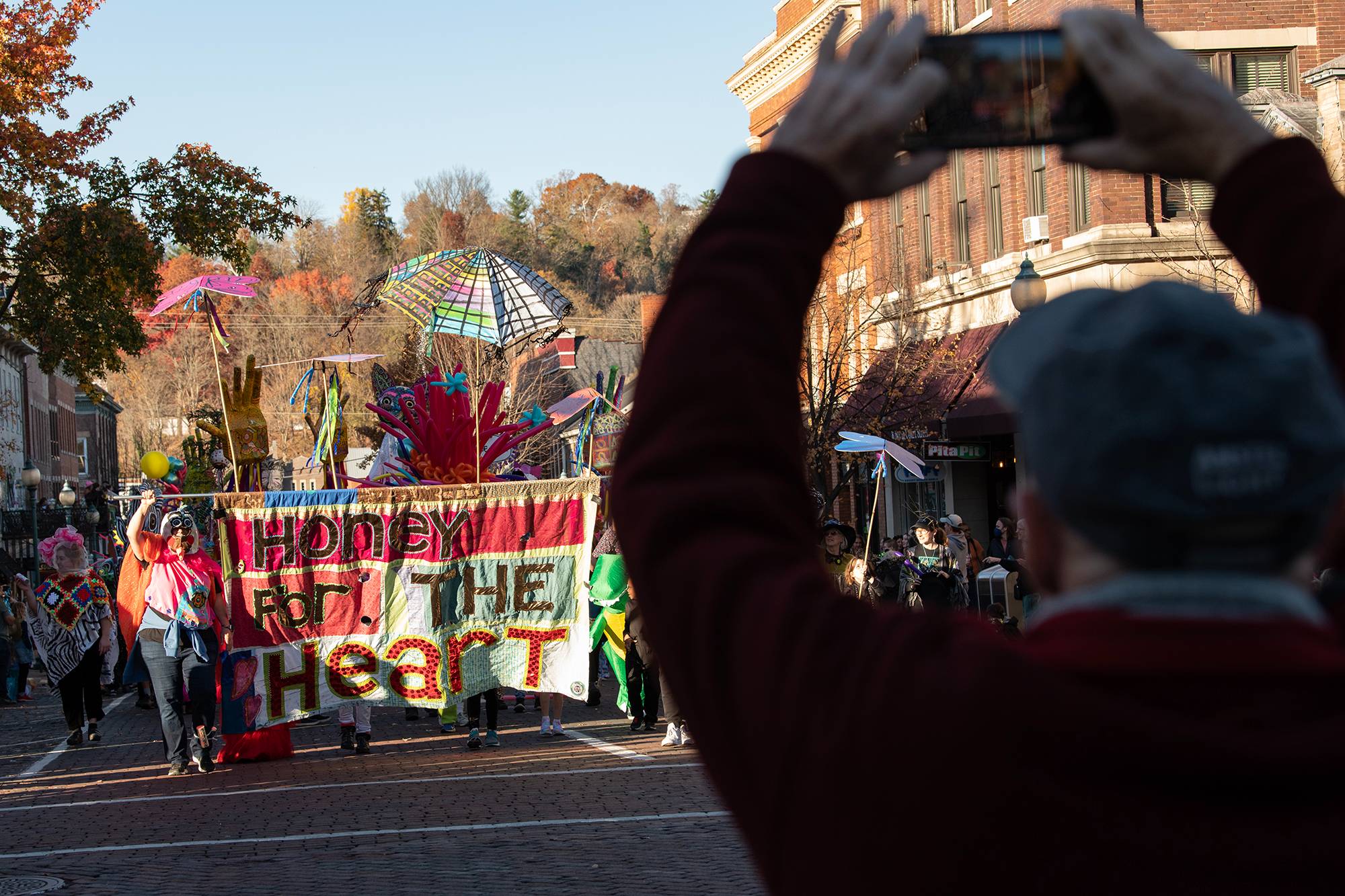 An audience member records the 2022 Honey for the Heart parade as participants walk and dance their way down Court Street in Athens, Ohio.