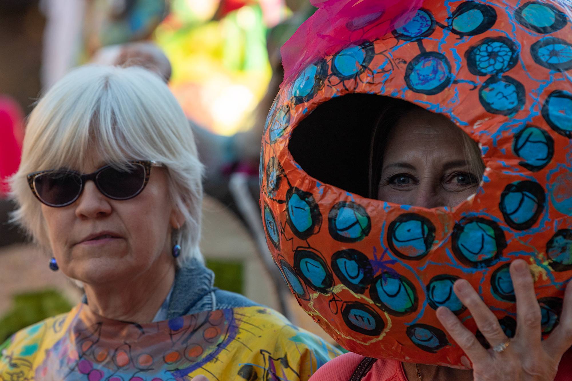 A member of the 2022 Honey for the Heart parade smiles behind a handmade paper mache mask.