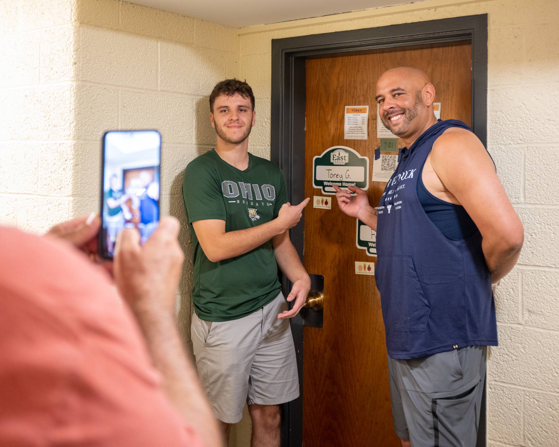 A first-year student poses for a photo just outside his new residence hall room on East Green