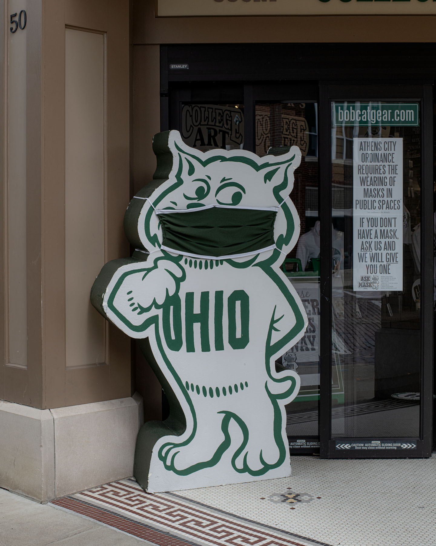 A cardboard cutout of the classic Rufus mascot stands outside a book store with a green cloth mask applied over it