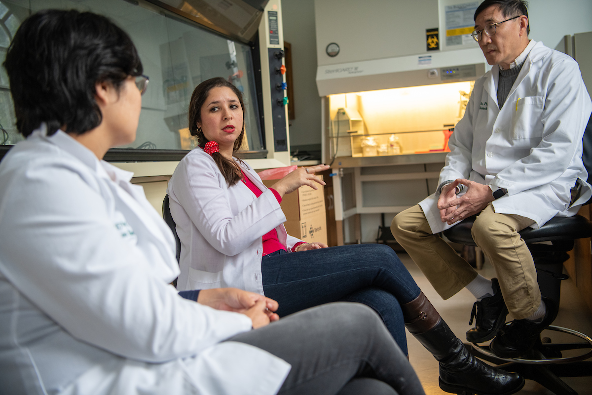 Graduate students in lab coats having a discussion with a professor