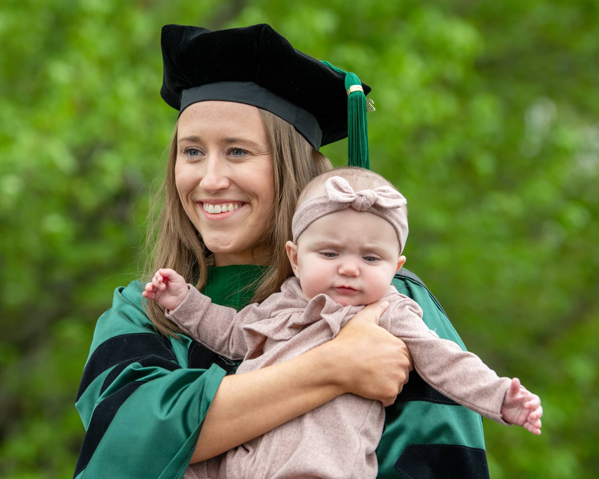 A Heritage College graduate poses for a photo with a baby following commencement.