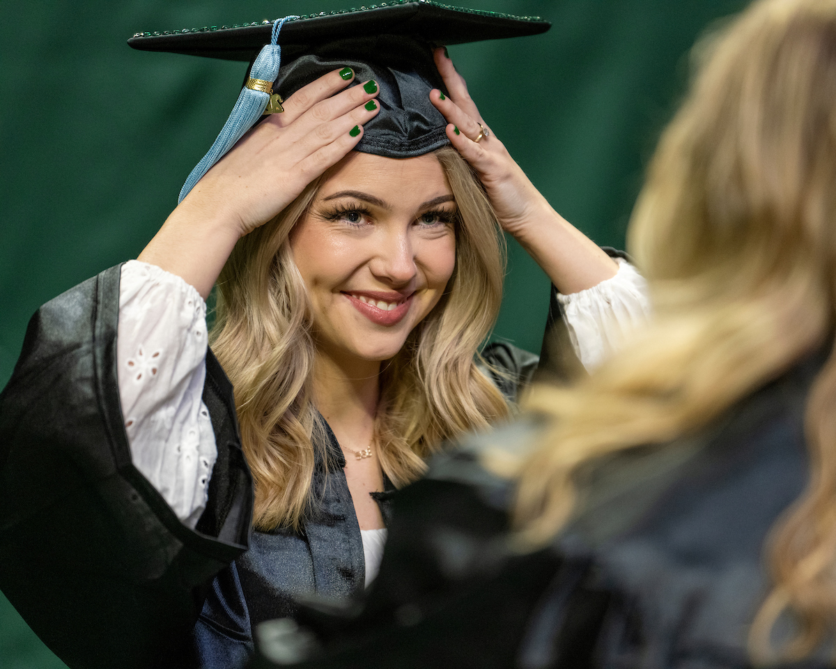 Female graduate adjusts graduation cap during commencement ceremony