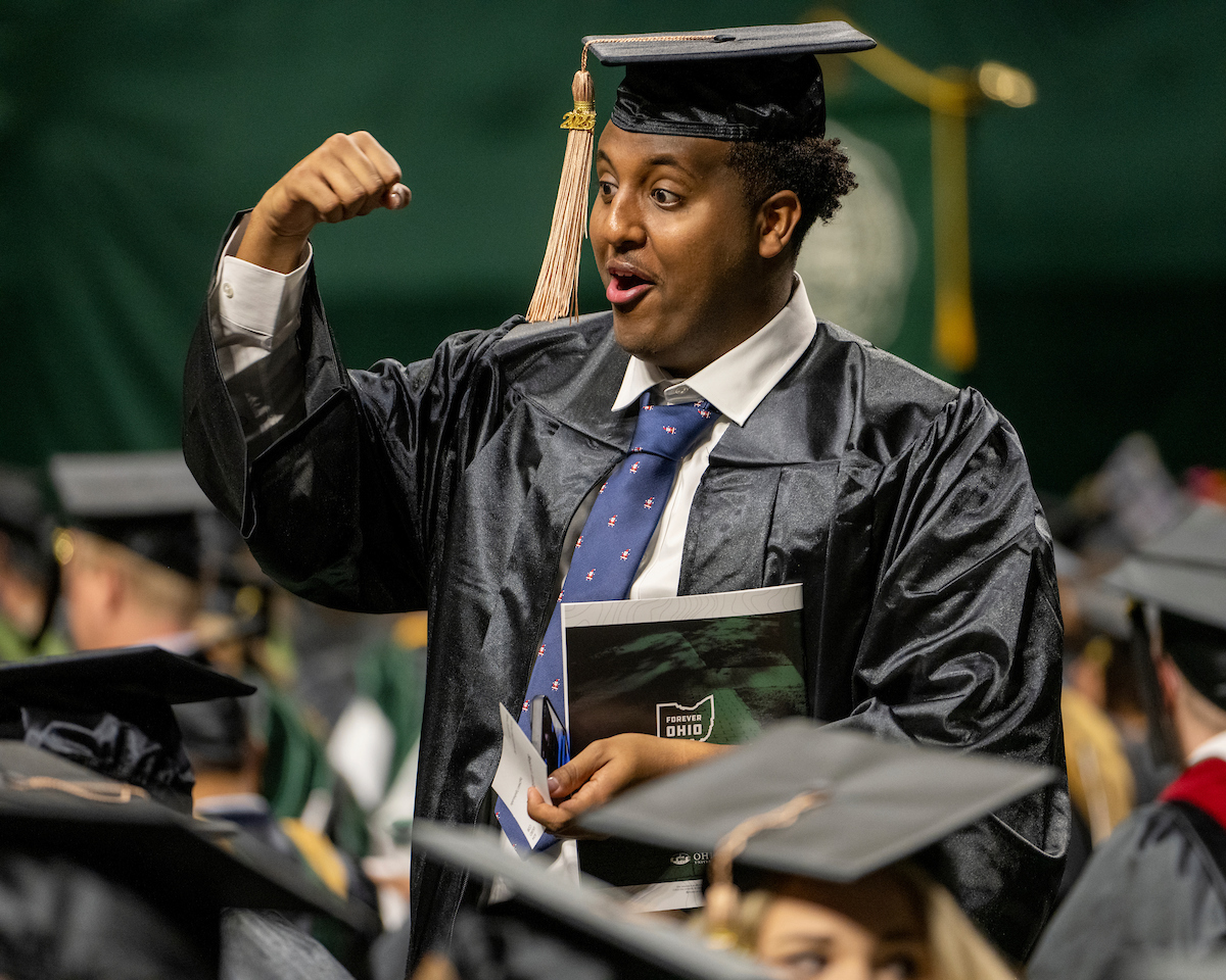 Male student gestures happily to the audience during Fall Commencement 